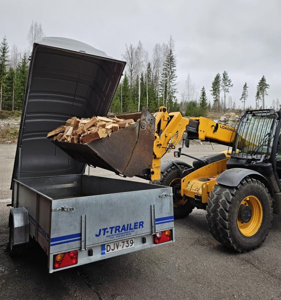 Traktori laittaa kauhalla polttopuita peräkärryyn.